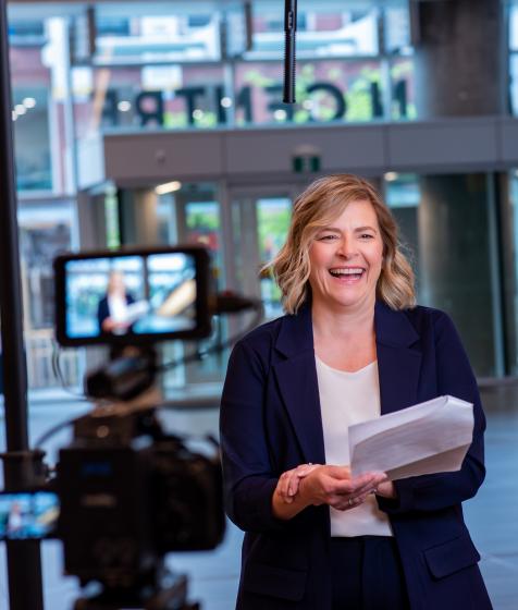 Photo shows Genaya Cameron, senior director of event operations, smiling while rehearsing lines in front of the TV camera while standing in the atrium of the halifax convention centre