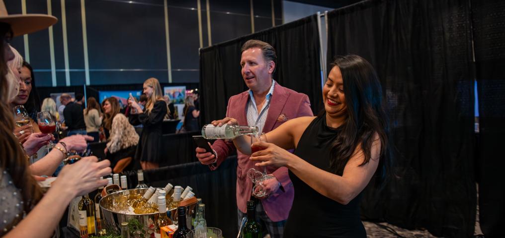 A sommelier pours wine into a glass as an outstretched hand reaches for it