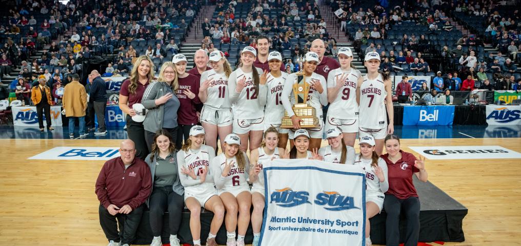the SMU Huskie Women's team holds the 2025 AUS Champion banner at centre court