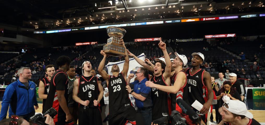 the 2018 champion team holds a trophy above their heads as they gather in a semi-circle cheering