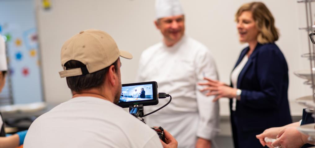 the Convention Centre chef shown demonstrating plating while a camera crew films
